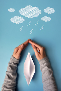 Bild på två händer som skyddar en pappersbåt från dåligt väder. Ska symbolisera båtförsäkring. 